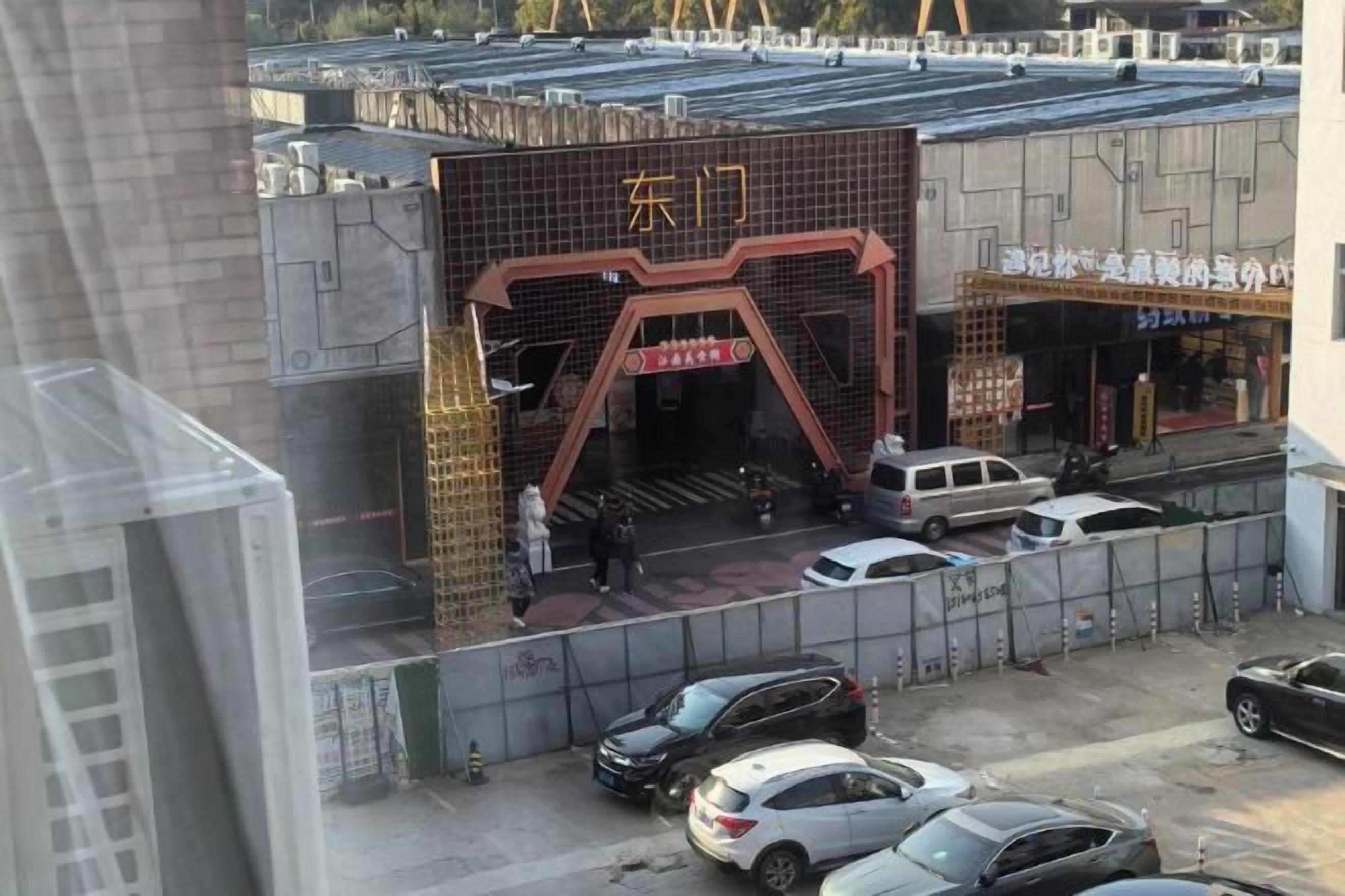 A building with a large entrance and a sign with Chinese characters. There are cars parked in front.
