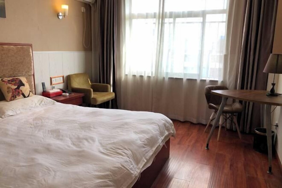 Habitació d'hotel amb un llit gran, escriptori, dues cadires, taula petita i finestra amb cortines.