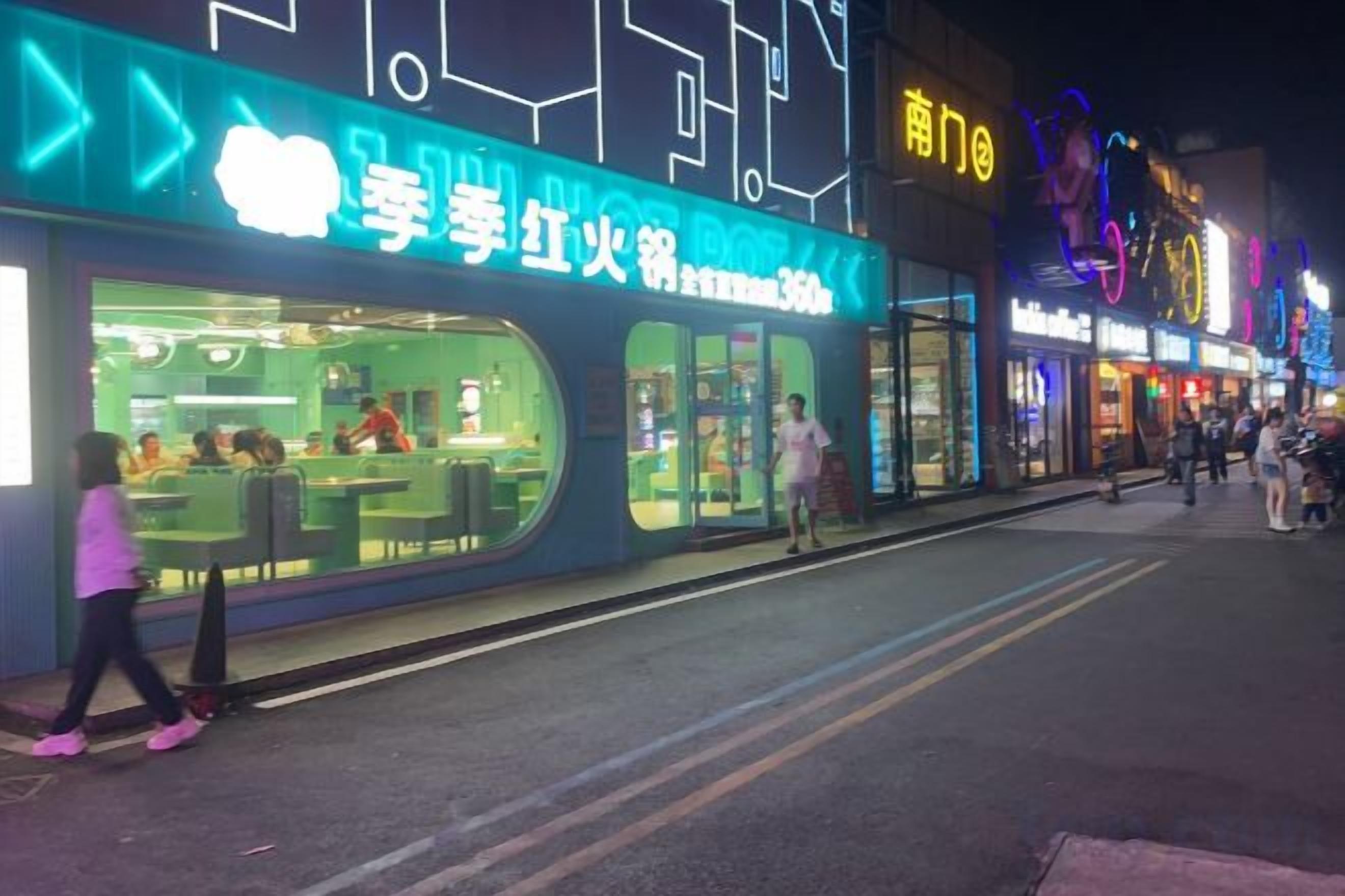 A brightly lit storefront with signage, a pedestrian walkway, and a street.
