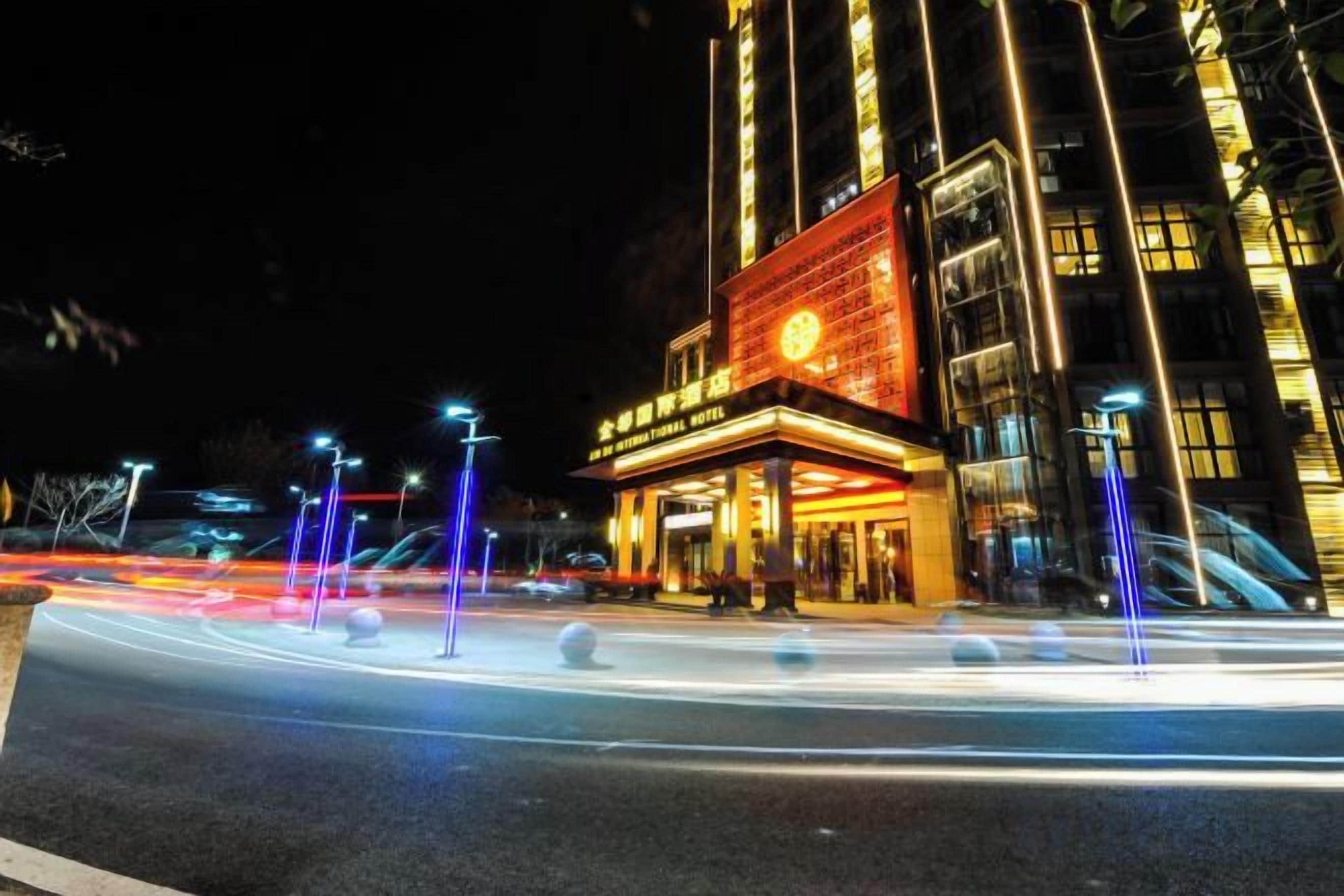 A building with a large illuminated sign, a vertical light pole, and a road with light trails.