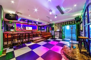 Un espace bar avec un sol à carreaux, des tabourets de bar et un décor illuminé par des néons.
