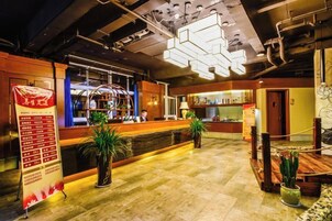 Un vestíbulo de hotel con una recepción, un letrero iluminado grande y plantas en macetas.