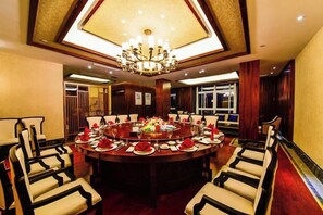 A round dining table set for a meal with chairs around it, a chandelier above, and a red carpet leading to the table.