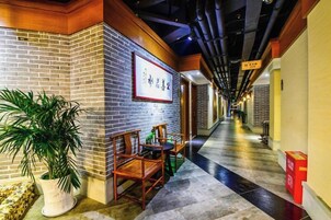A corridor with brick walls, a framed sign, a potted plant, and wooden chairs.