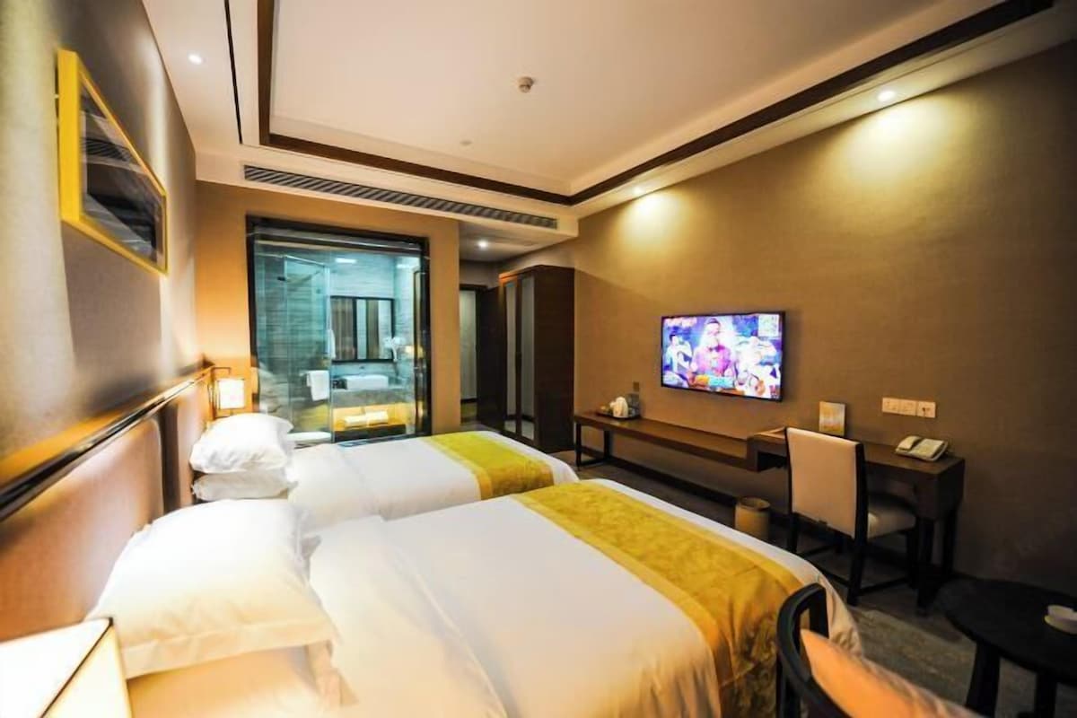 A hotel room with two beds, a TV, a desk, and a chair.