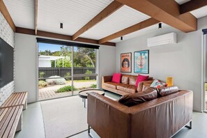 A modern living room with a leather sofa, a wooden bench, and a large sliding glass door leading to an outdoor area.