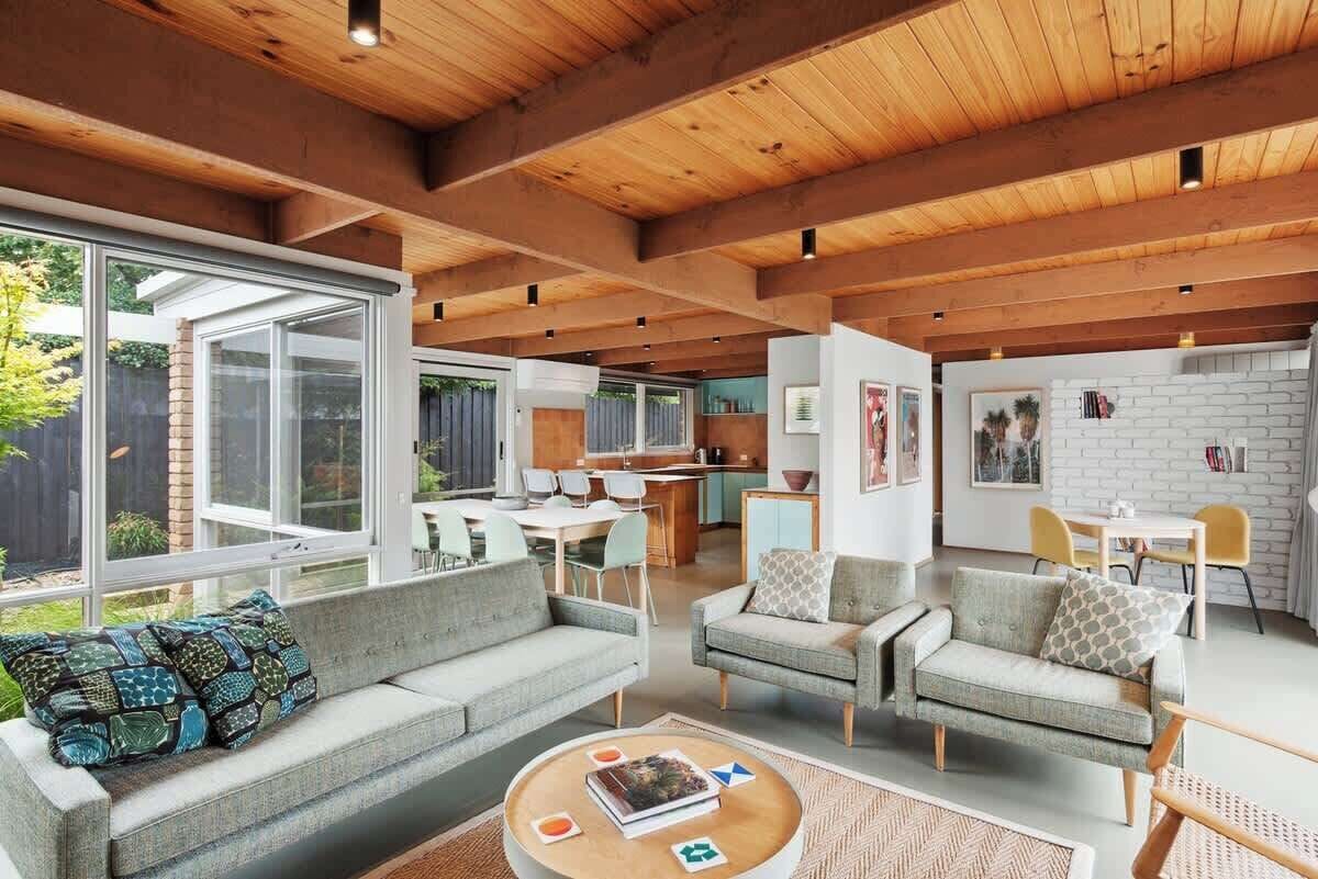 A spacious living area with a high ceiling, large windows, and a kitchen in the background.