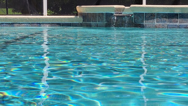 Ein klarer Pool mit gefliestem Rand und einer kleinen Wasserfallanlage.