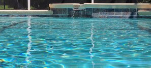 Ein klarer Pool mit gefliestem Rand und einer kleinen Wasserfallanlage.