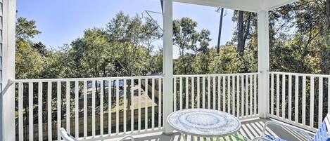 A covered outdoor patio with a round table and blue chairs, surrounded by white railings and a view of trees and a fence.