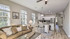 Un salon spacieux avec un grand canapé, une table basse et un coin repas comprenant des chaises, et une cuisine en arrière-plan.