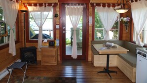 A cozy cabin interior with a wooden interior, a dining table, a bench, a stove, and a window with curtains.