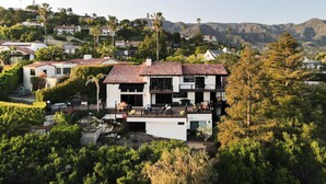 A modern two-story house with a red-tiled roof, surrounded by lush greenery and mountains in the background. - New! Breathtaking Patio Ocean Views, Private Riviera Retreat 30 Day Minimum (Santa Barbara)