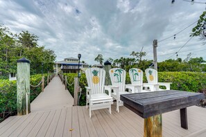 A wooden deck with white chairs and a bench, leading to a house with a blue roof. - Luxury Key Largo Home w/ Guest House & Pool! (Key Largo)