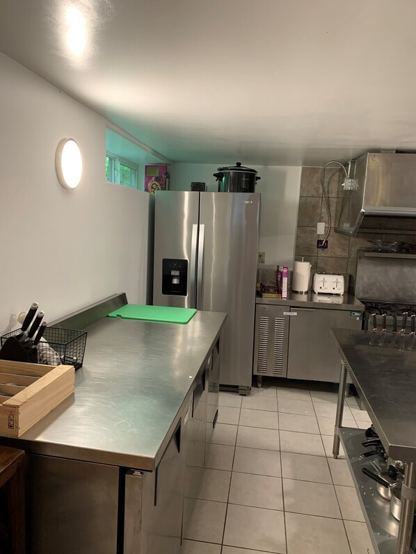 A modern kitchen with stainless steel appliances, a green cutting board, and a knife block. - New Denver Lodge – Relax, Unwind & Reconnect (New Denver)