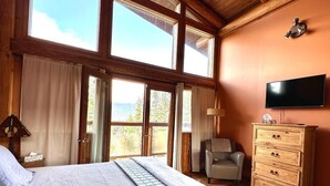 A bedroom with a large bed, a wooden dresser, a television, and a chair. - New Denver Lodge – Relax, Unwind & Reconnect (New Denver)