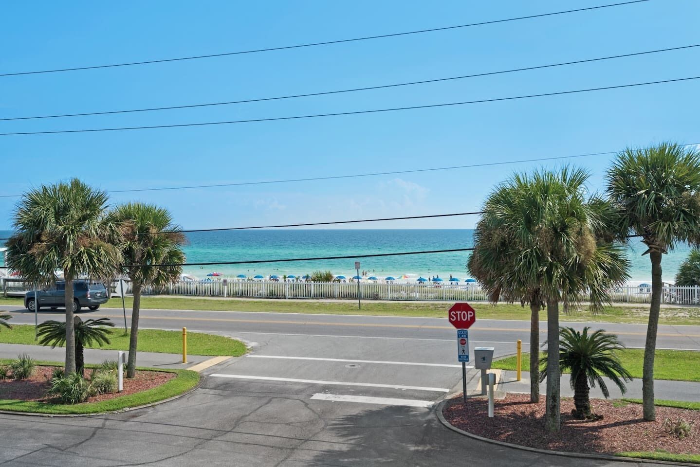 A beachside intersection with a stop sign, palm trees, and a view of the ocean.