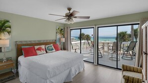 A bedroom with a bed, a ceiling fan, a balcony with chairs, and a view of the ocean. - Gulf Views*Private Beach*Dog Friendly*Beach Gear (Destin)