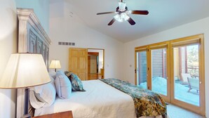 A bedroom with a bed, two bedside lamps, a ceiling fan, and a sliding glass door leading to an outdoor area. - Angel Fire Country Club | Views | Camp Happy (Angel Fire)