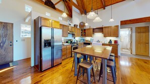 A modern kitchen with wooden cabinets, stainless steel appliances, and a central island with stools. - Angel Fire Country Club | Views | Camp Happy (Angel Fire)