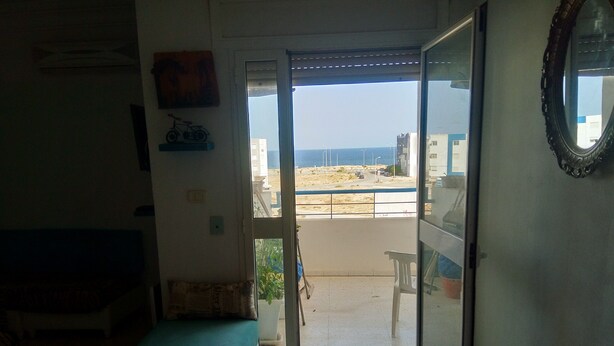 Una habitación con vista al mar, un balcón con mesa y sillas, y una puerta que da al exterior.