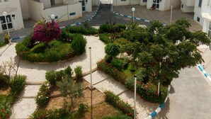Un edificio residencial de varios pisos con un patio central que cuenta con jardines ajardinados, un camino pavimentado y una bordeadora azul y blanca.
