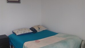 Una habitación pequeña y sencilla con una cama, una mesita de noche y un cuadro en la pared.