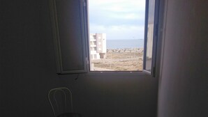 Una habitación pequeña con una mesa, dos sillas, un ventanal con vistas a edificios y una masa de agua, y una puerta.