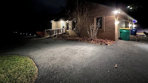 Un bâtiment illuminé la nuit, avec un éclairage extérieur, une allée pavée et une petite pelouse.