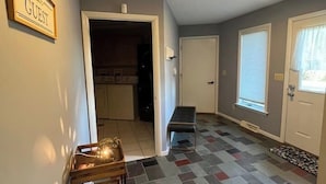 Un couloir avec une pancarte indiquant « VISITEURS », un banc, un sol à motifs et une porte donnant sur une cuisine.