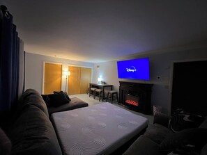 Camera d'albergo con una grande TV a schermo piatto, un caminetto, un divano, un tavolo da pranzo con sedie e un angolo cottura.