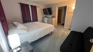 Une chambre à coucher avec un lit, une commode, un téléviseur et un bureau avec une lampe.