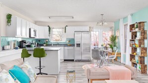 A modern kitchen with white cabinets, a stainless steel refrigerator, and a dining area with a table and chairs.