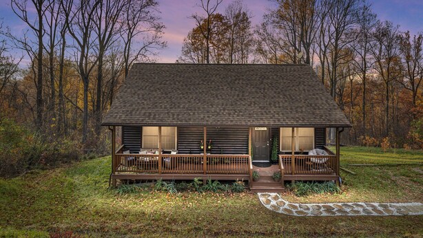 A log cabin with a porch, a stone pathway, and a forested backdrop.