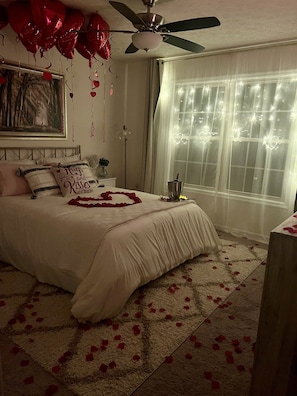 Une chambre à coucher avec un lit, un ventilateur de plafond, une fenêtre avec des rideaux et un tableau encadré au mur.