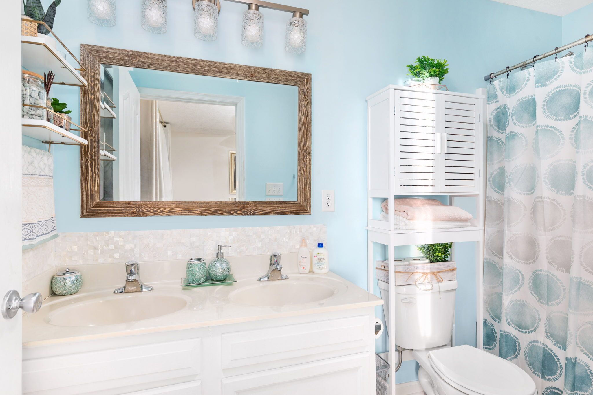 A bathroom with a double sink, a large mirror, a toilet, and a shower curtain.