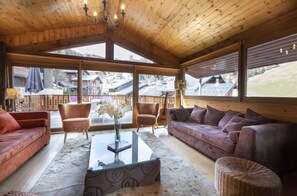 A spacious living room with wooden ceilings, large windows, and a view of surrounding buildings. - Chalet Individuel Accès Direct Au Domaine Skiable! (La Plagne-Tarentaise)