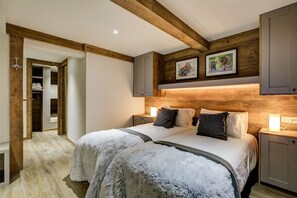 A bedroom with two beds, wooden beams, a closet, and framed pictures on the wall.
