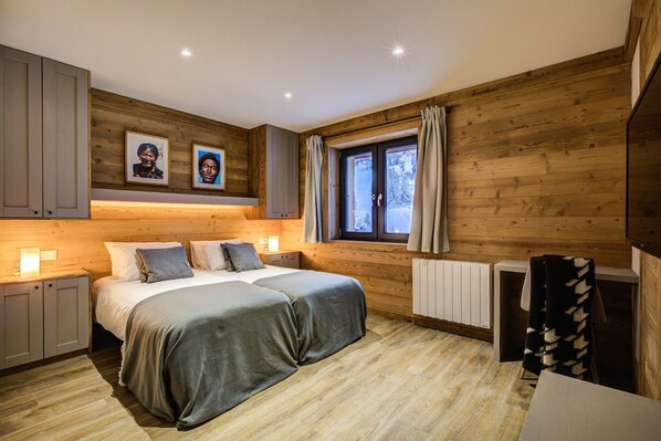 A cozy bedroom with a wooden interior, a large bed, a window with curtains, and a radiator.