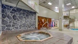 Un espace de bien-être doté d’un mur en pierre, d’un jacuzzi et d’un escalier menant à un autre niveau.