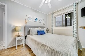 Une chambre à coucher avec un lit, une table de chevet, une lampe et une œuvre d’art accrochée au mur.