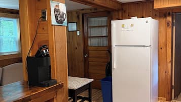 A compact kitchen with wooden walls, a white refrigerator, a coffee maker, and a window with blinds.