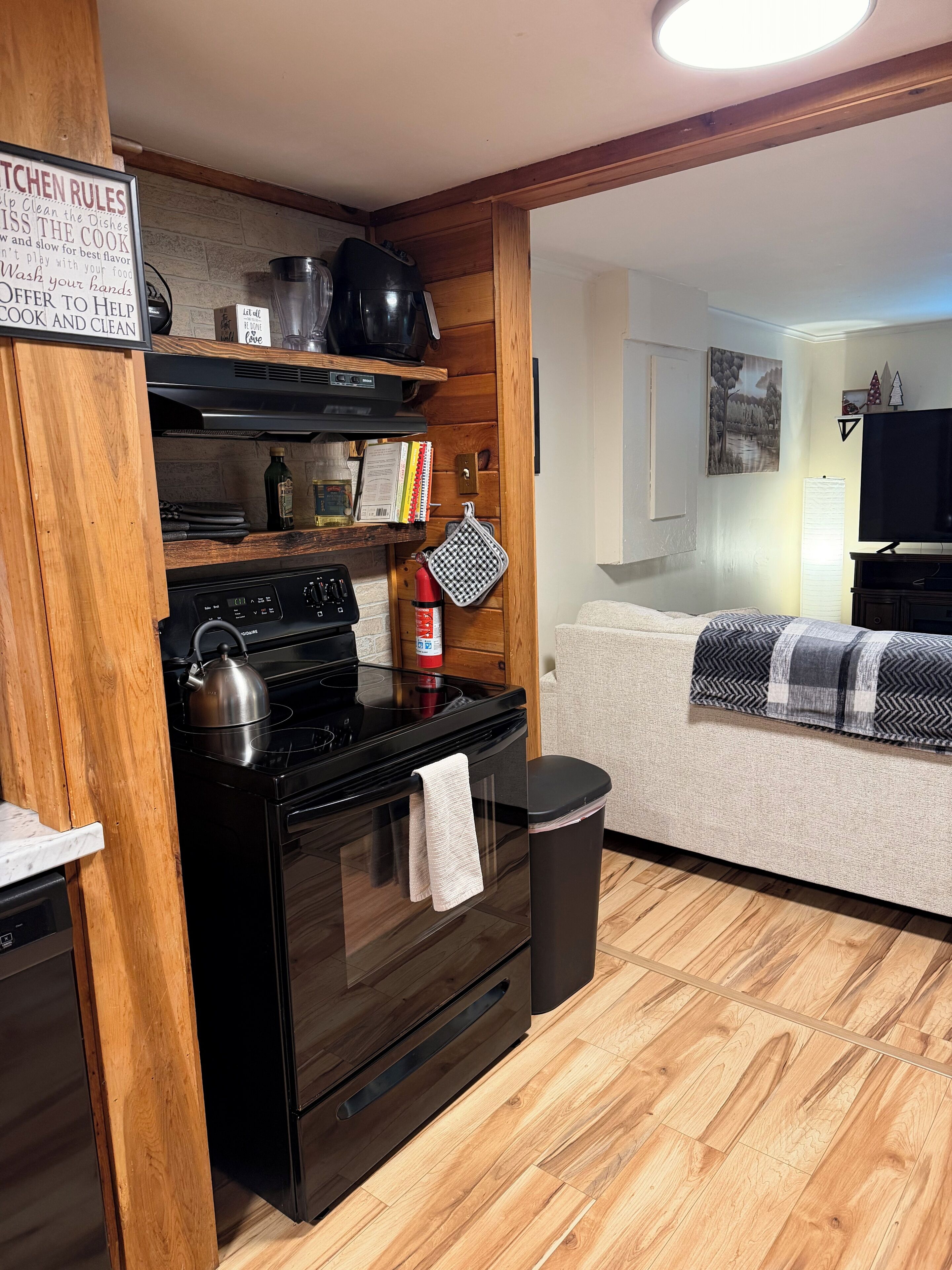 A compact kitchen with a stove, oven, and a sign with kitchen rules.