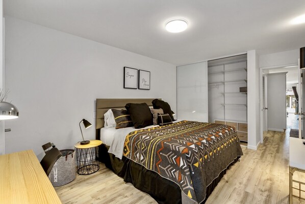 A modern bedroom with a large bed, a bedside table, a lamp, and a storage unit.