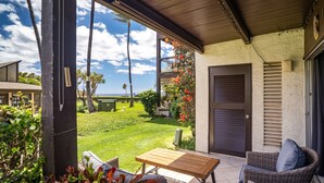 Un patio techado con una mesa y sillas de mimbre, con vista a un césped cuidado y al océano.