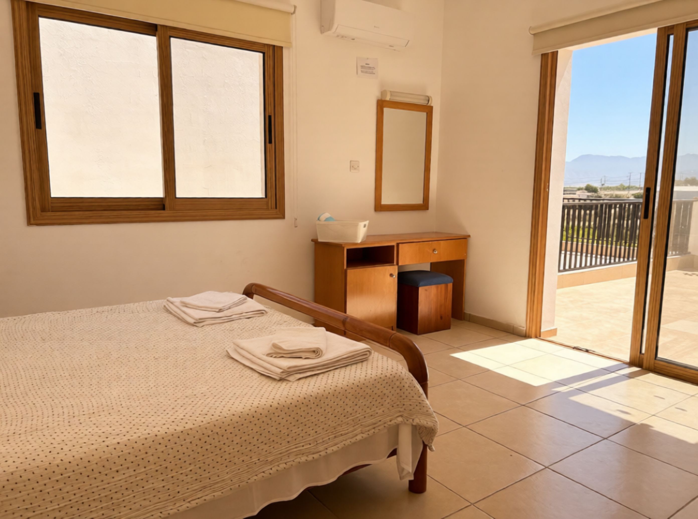 Een slaapkamer met een bed, een houten bureau, een spiegel en uitzicht op het omliggende landschap.