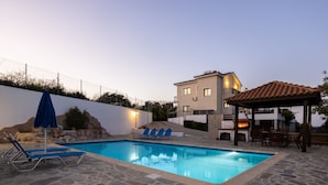 A swimming pool with lounge chairs and a pergola, surrounded by stone flooring and a white wall. - Villa Ira Finiki: Private pool and gardens, A/C, Wi Fi, sea views (Latchi)