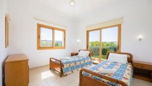 A bedroom with two wooden beds, a wooden dresser, and a large window offering a view of greenery. - Villa Ira Finiki: Private pool and gardens, A/C, Wi Fi, sea views (Latchi)