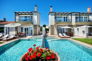 Une maison moderne à deux étages, dotée d’une piscine, de chaises longues et d’un jardin.