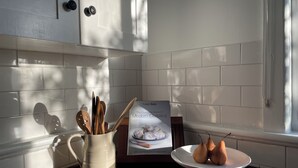 A kitchen with white cabinets, a wooden countertop, a white pitcher with wooden utensils, a cookbook, and a white plate with pears. - When a little white house in the country is all that is required! (Maffra)